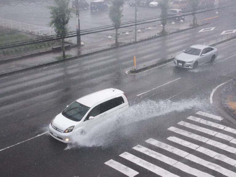 雨天の中、勢いよく水を跳ねさせて走行するクルマの写真