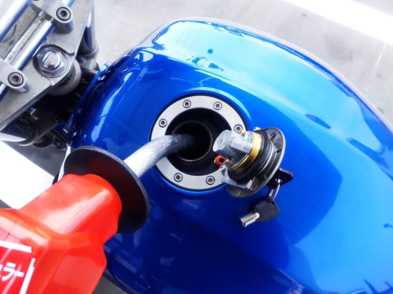 青いバイクに給油するライダーの写真