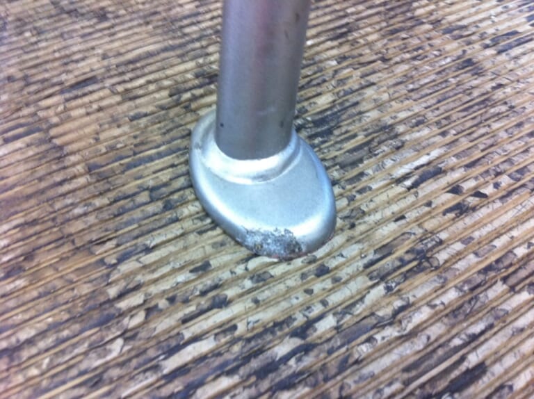 バイクサイドスタンドの下に一枚の板を敷いている写真|「スタンドがめり込んでバイクが倒れた…」夏場のバイク駐車、アスファルト路面には要注意