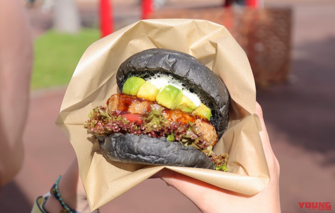 黒いバンズが特徴的なハンバーガーを試食する女性|【MotoGP日本GP 10/4~6開催!】会場限定グルメをひと足先にレポート!