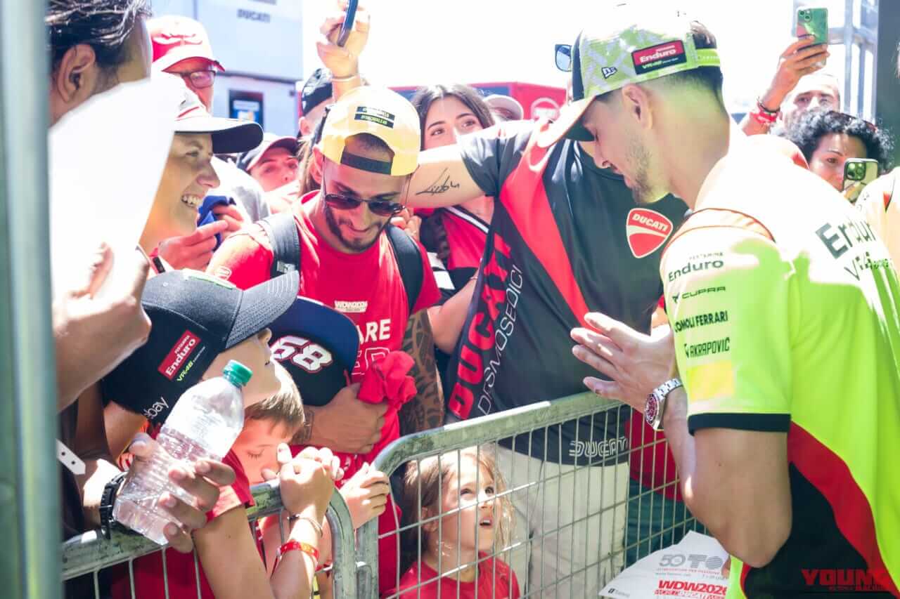 ピット裏に詰めかけたファンのサインに応じているのは、MotoGPライダーのディッジャことファビオ・ディ・ジャンアントニオ。この後、着ていたチームシャツを脱いでサインをし、少年にプレゼントした。｜来場12万人、パレードは驚異の18km！ドゥカティ100周年記念の『WDW2026』が史上最高のド迫力【マルケス、バニャイア、ストーナーも】