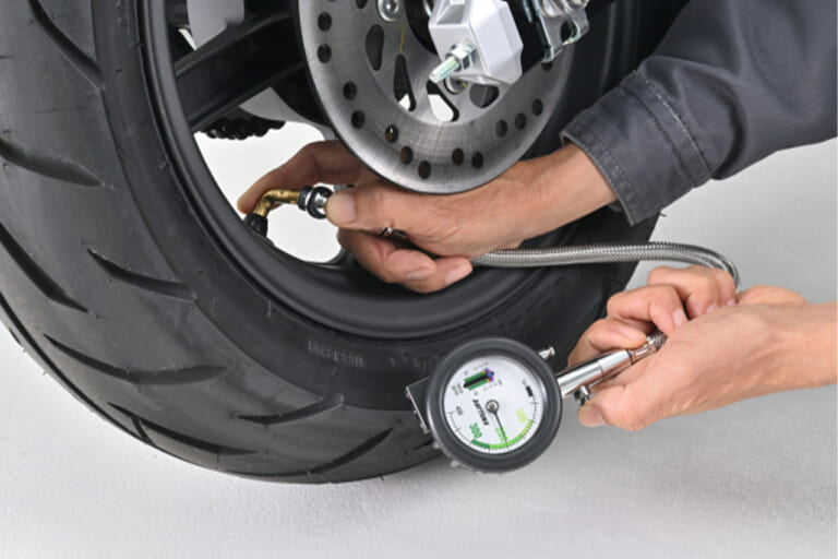 デイトナのメッシュホース付きエアゲージ デプスゲージ付きで、バイクの後輪の空気圧を計測している写真｜「それ、ヤバいですよ…」夏場のパンパンタイヤの恐怖…。高温が続くこの季節だからこそ、定期的な空気圧チェックは欠かせない！［デイトナ・メッシュホース付きエアゲージ デプスゲージ付き］