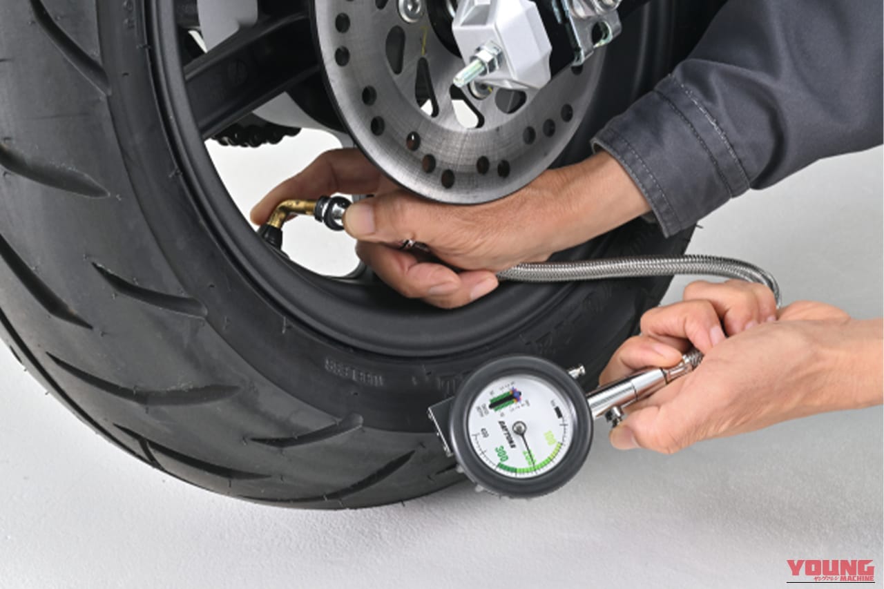 デイトナのメッシュホース付きエアゲージ デプスゲージ付きで、バイクの後輪の空気圧を計測している写真｜「それ、ヤバいですよ…」夏場のパンパンタイヤの恐怖…。高温が続くこの季節だからこそ、定期的な空気圧チェックは欠かせない！［デイトナ・メッシュホース付きエアゲージ デプスゲージ付き］