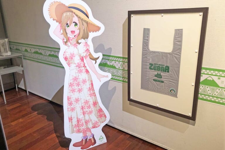 犬山あおい等身大パネルとスーパーゼブラのレジ袋｜【ゆるキャン△と山梨▲】ビーノ『ゆるキャン△』コラボVer.展示や録り下ろしボイスも！山梨県立博物館の企画展現地レポート＆2027年TVアニメ4期情報